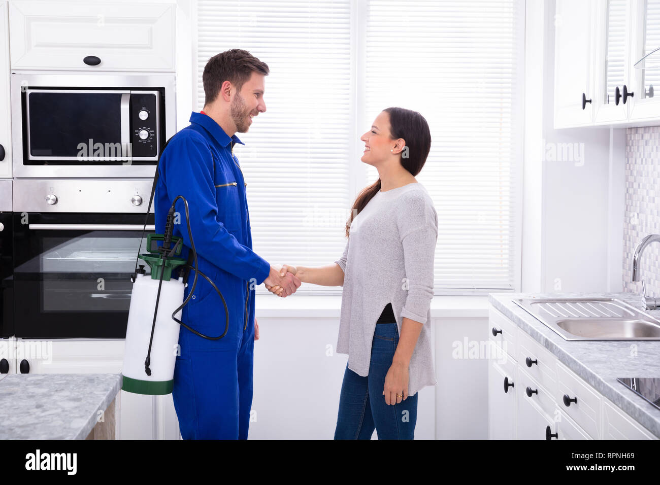 Woman Showing Thumbs Up With Pest Control Worker Standing In Kitchen Stock Photo