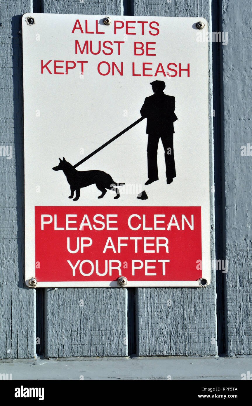 A Red, Black and White sign that reads 'All Pets Must Be On Leash' and Please Clean Up After Your Pet. There is a silhouette of a Man walking a dog. Stock Photo