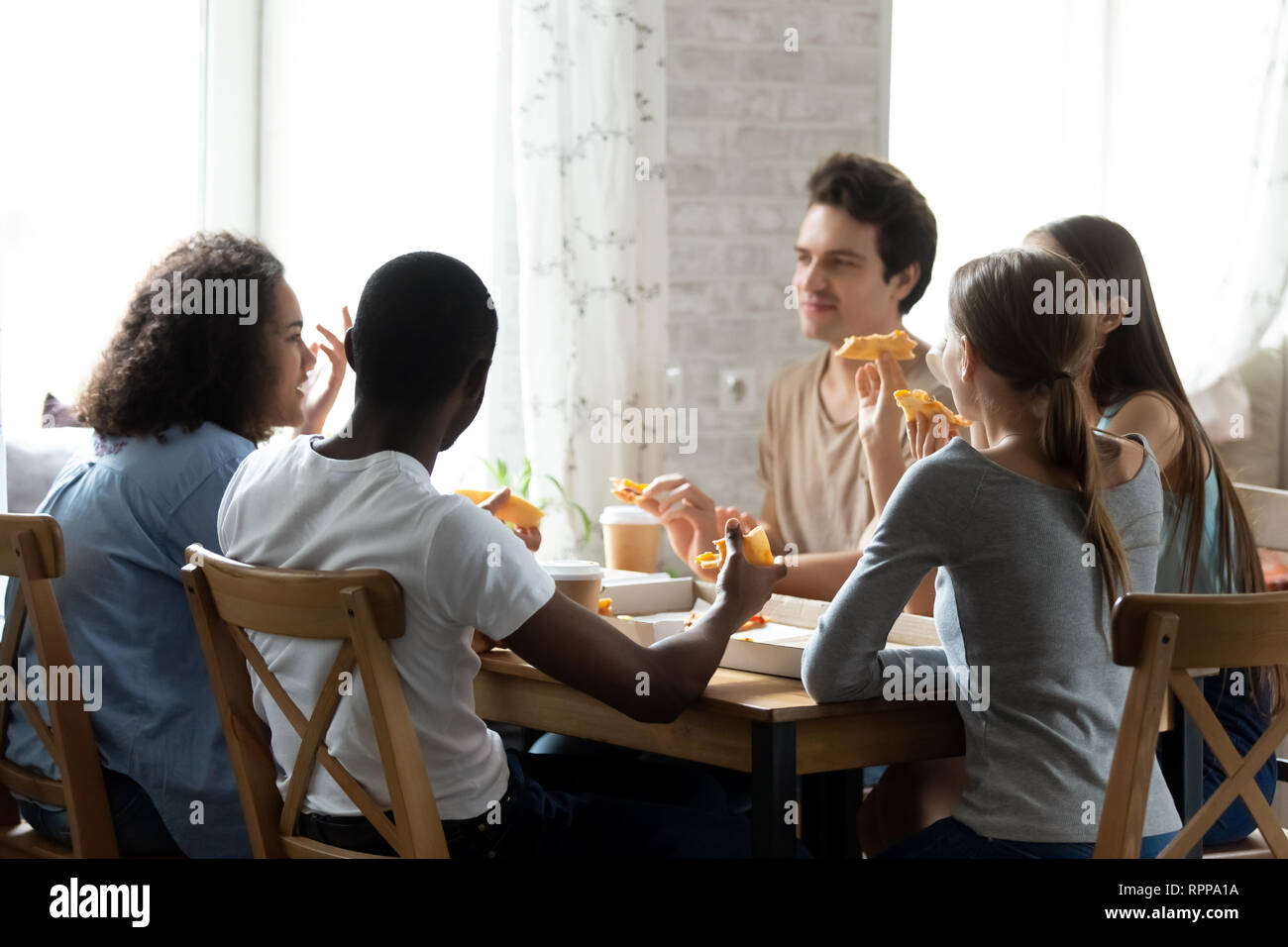 Multiracial friends having conversation and eating pizza in cafe Stock Photo