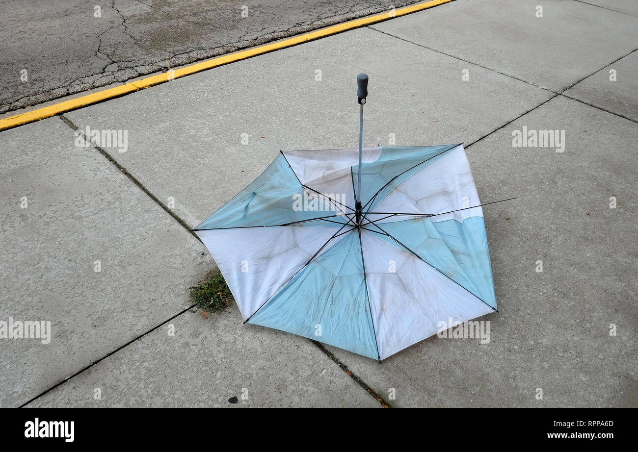 A wind damaged umbrella lays on a concrete sidewalk in the U.S.A. Stock Photo