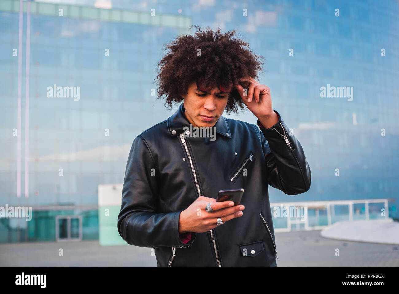 Stylish young man with afro hairstyle messaging with a smart phone in urban modern background, concept communication Stock Photo