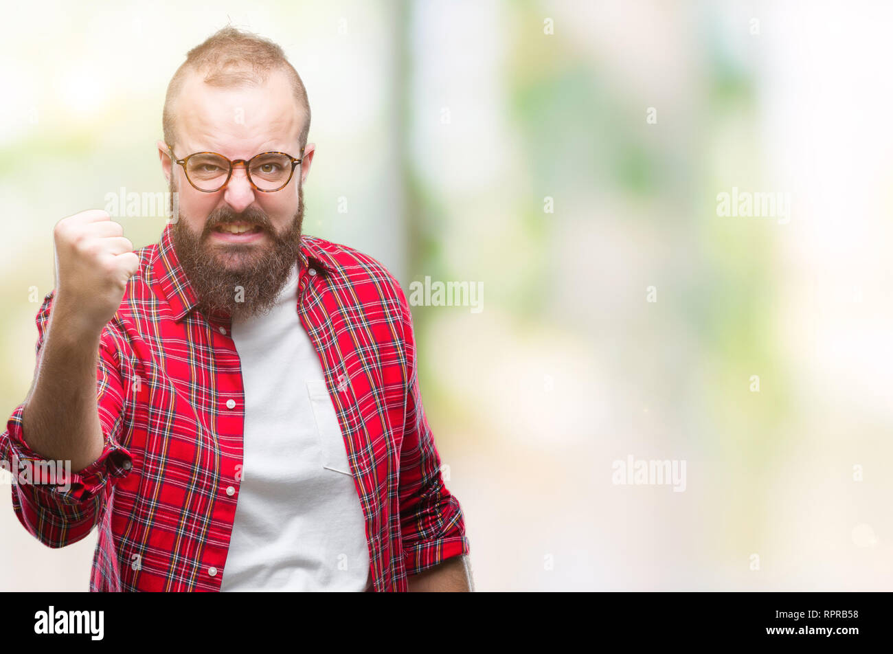 Young caucasian hipster man wearing glasses over isolated background angry and mad raising fist frustrated and furious while shouting with anger. Rage Stock Photo