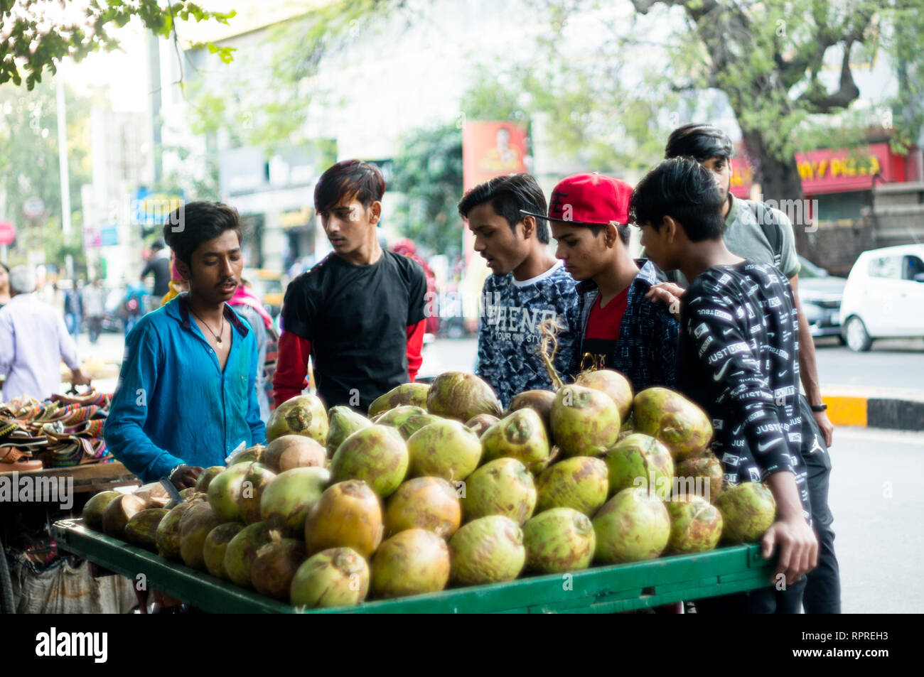Coconut vendor and cart surrounded by people eager to drink Stock Photo