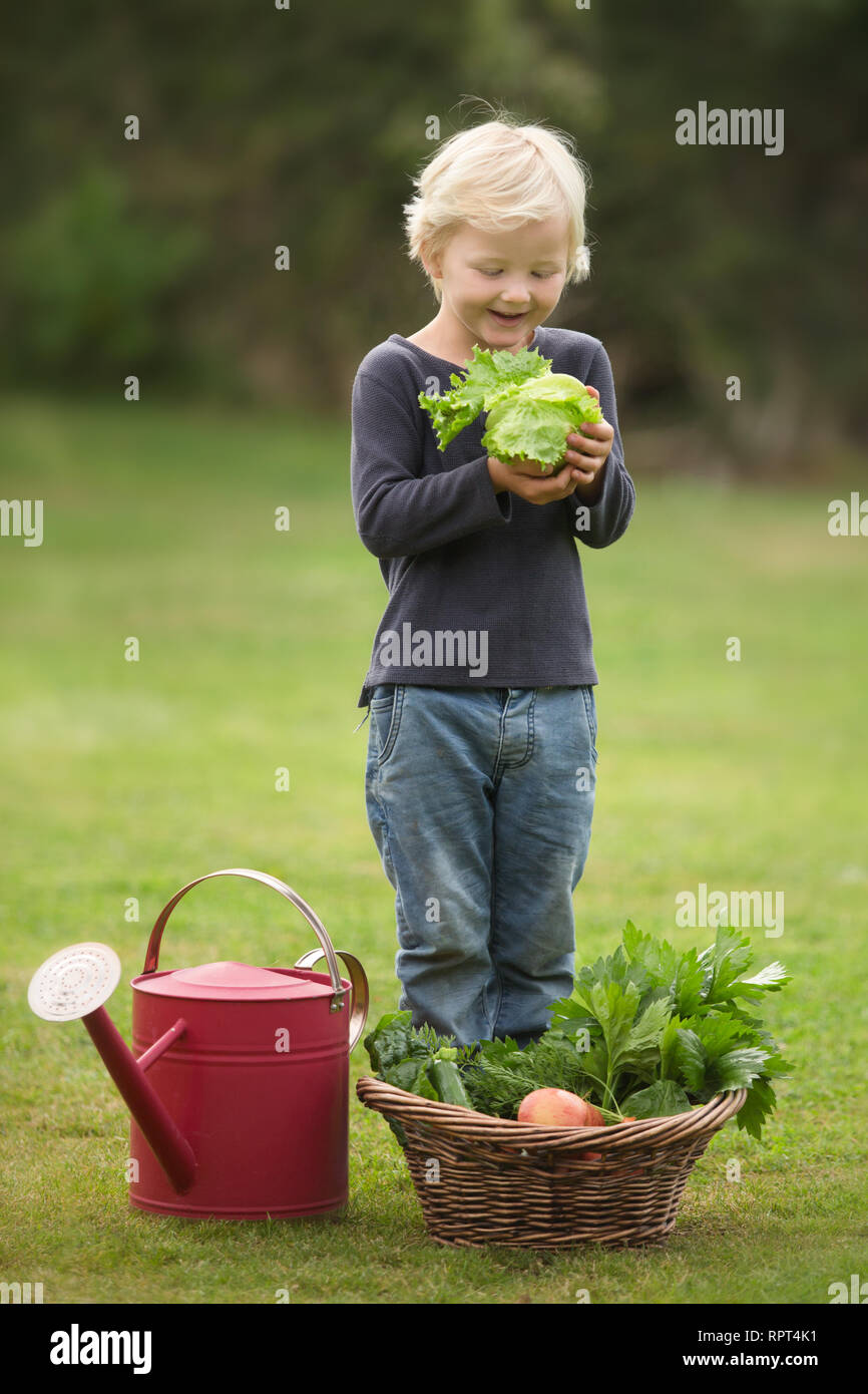 A blonde child happily shows off his harvest of fruit and vegetables Stock Photo
