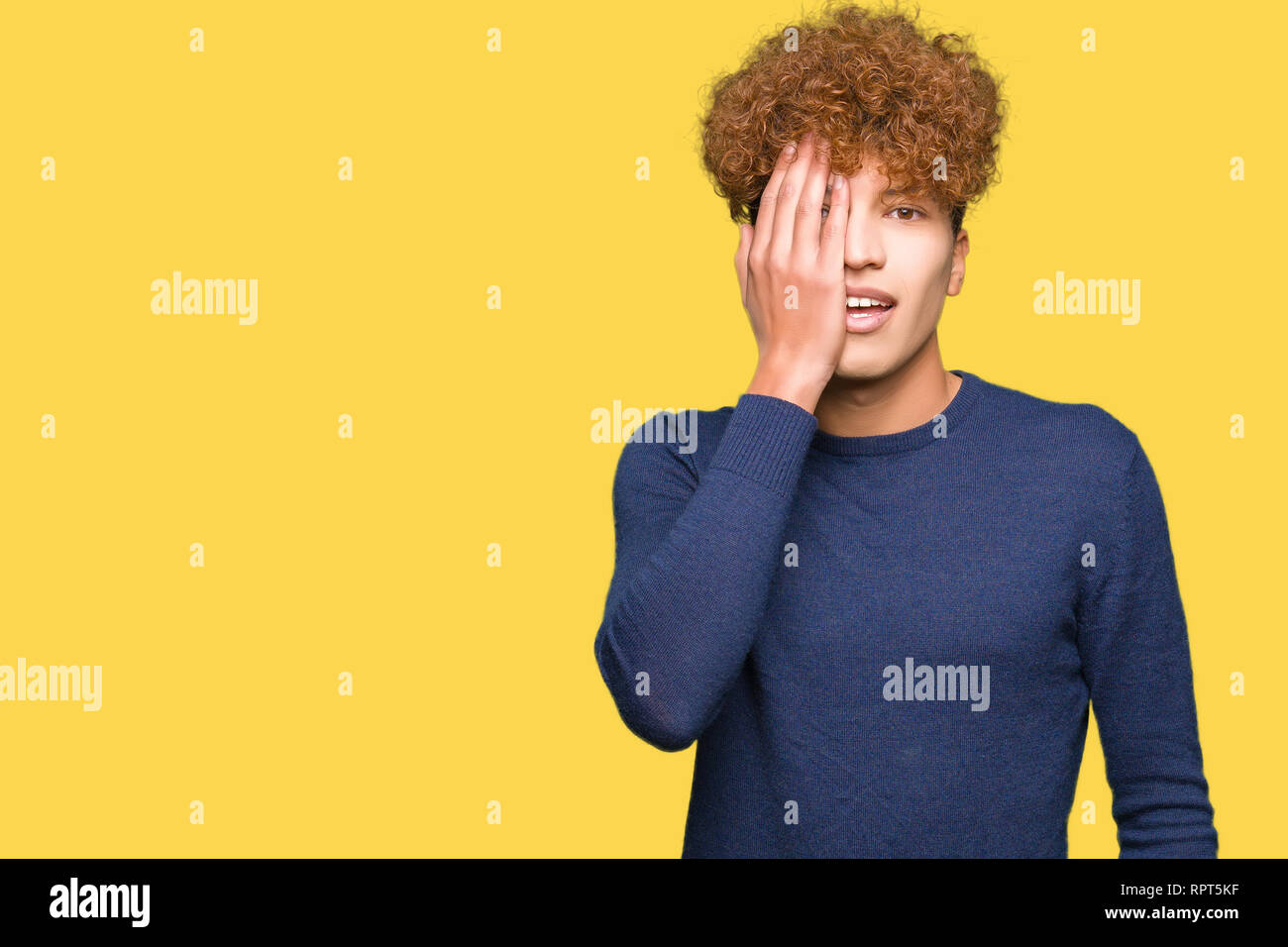 Young handsome man with afro hair covering one eye with hand with