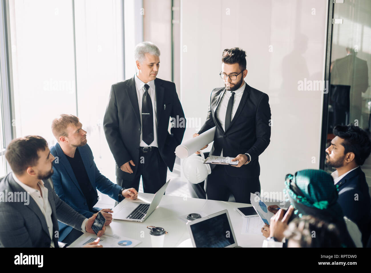 Male caucasian employee presents business strategy on white paper shift to top managers of his company in boardroom. Chief is standing beside, all the Stock Photo