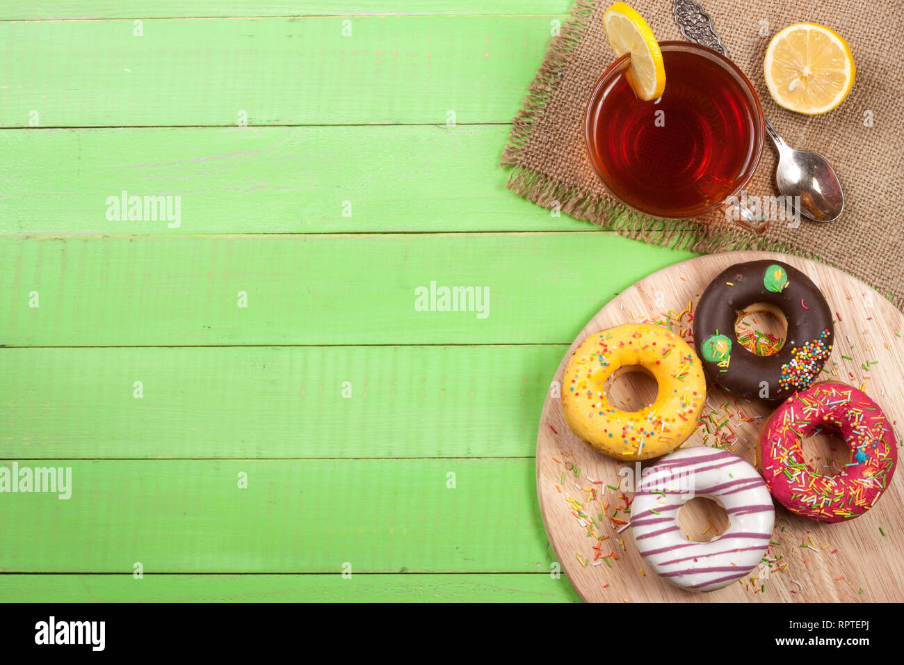 glazed donuts with a cup of tea on a green wooden background with copy ...