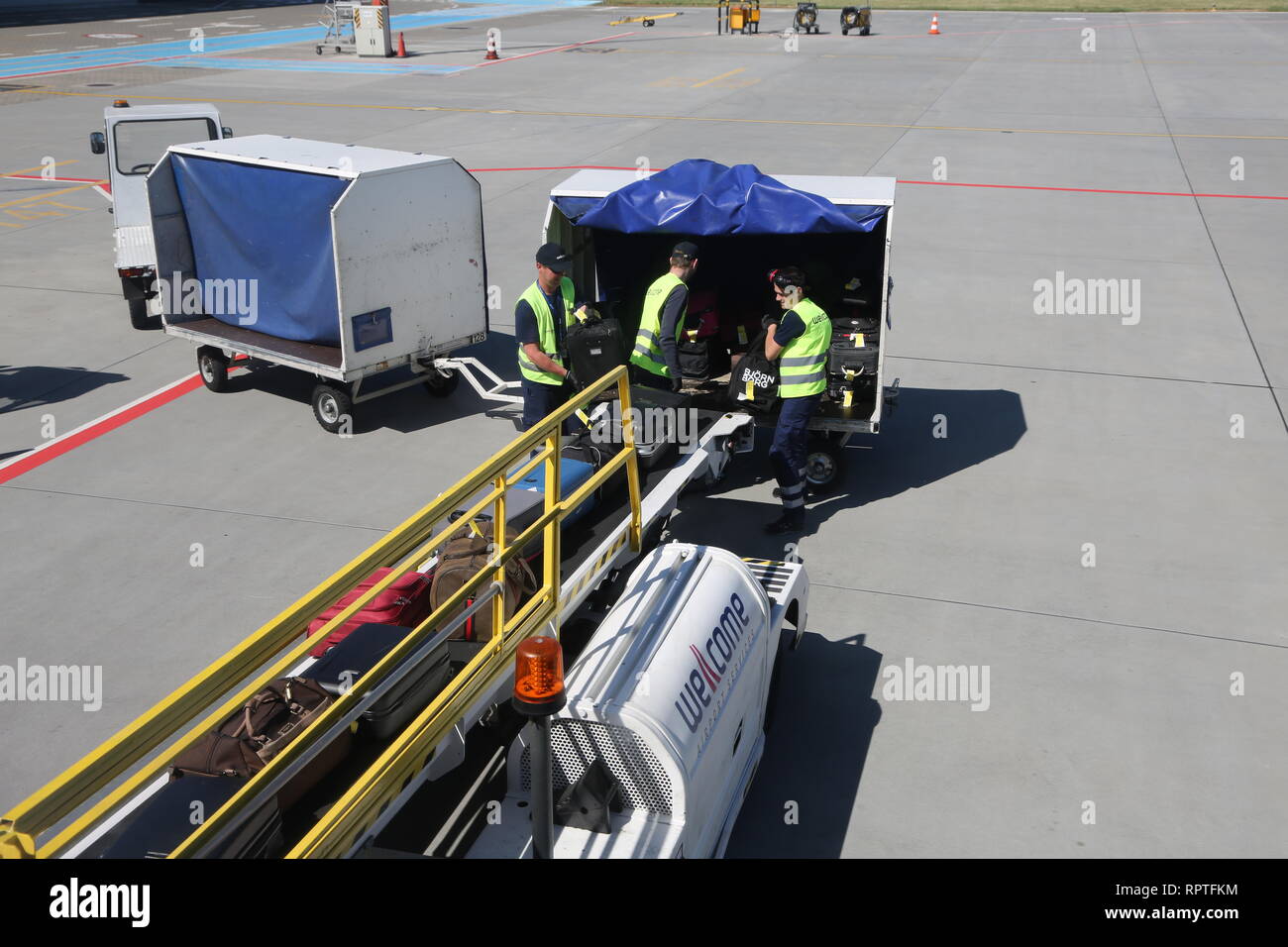 Baggage Handlers working at Poznan Lawica Airport place bags onto the conveyor belt loading a Ryanair Boeing 737. Stock Photo