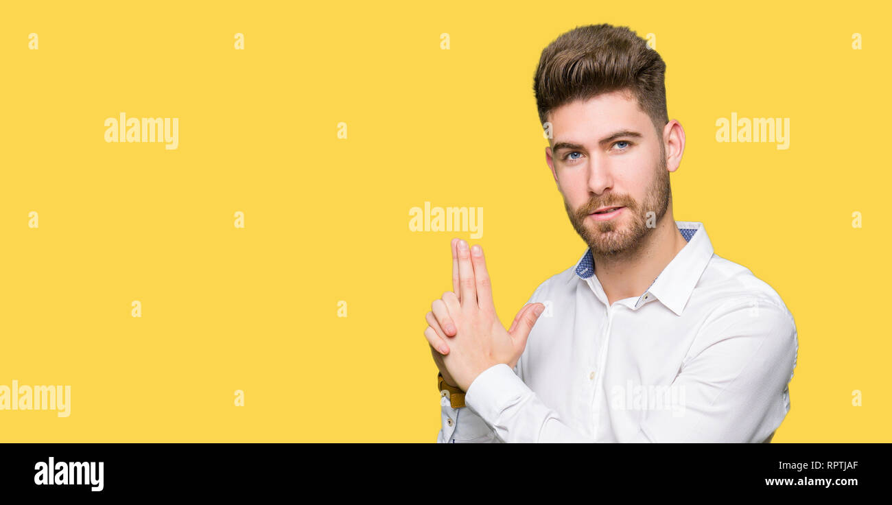 Young handsome business man Holding symbolic gun with hand gesture, playing killing shooting weapons, angry face Stock Photo