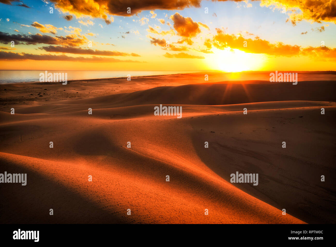 Rays of sun over horizon at sunset in arid desert sand dunes of Stockton beach on Australian pacific coast with warm sunlight casting shades between s Stock Photo
