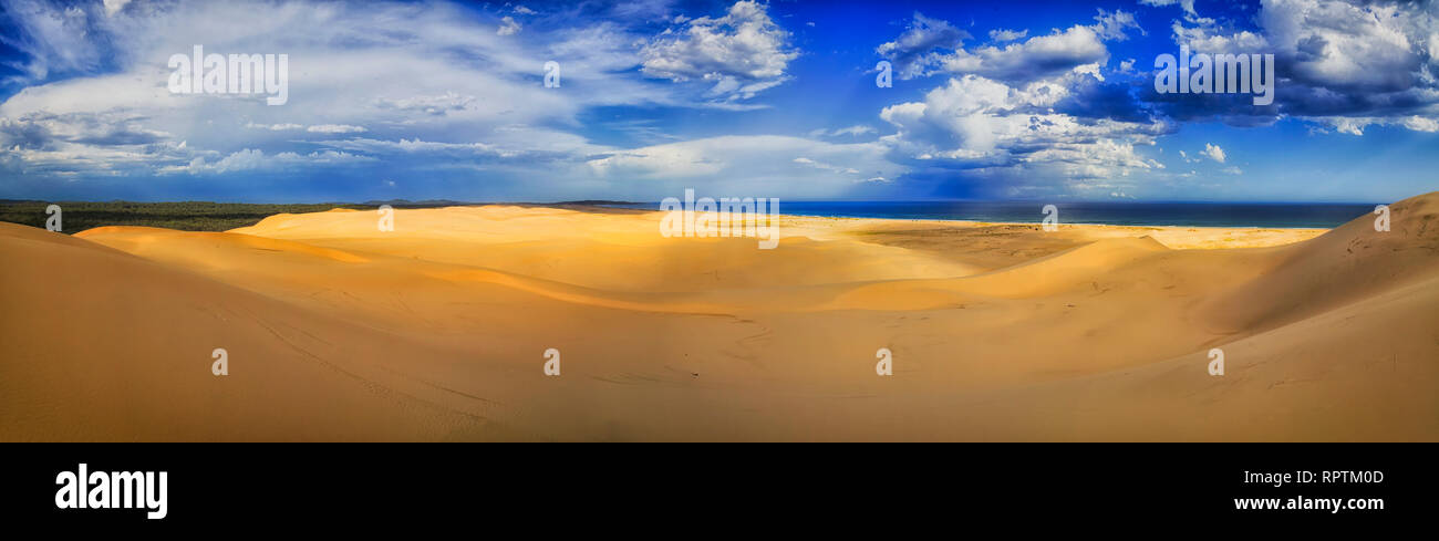 Bright clean sandy arid desert of sand dunes in Stockton beach under blue sky with clouds as wide panorama from Pacific ocean to gum-tree woods. Stock Photo