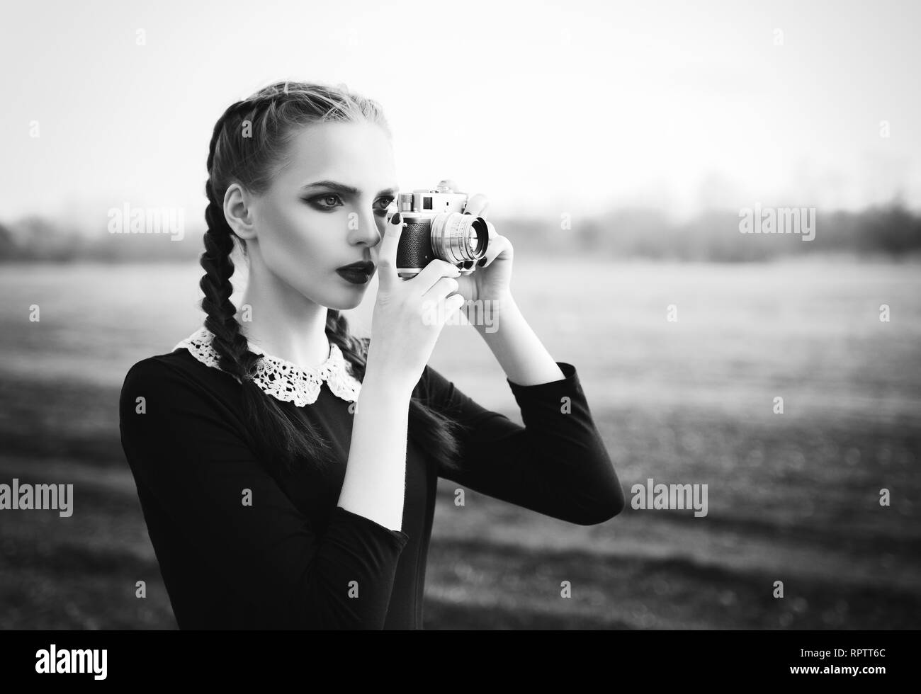 Beautiful young girl shooting by the old classic film camera. Outdoor portrait, black and white Stock Photo