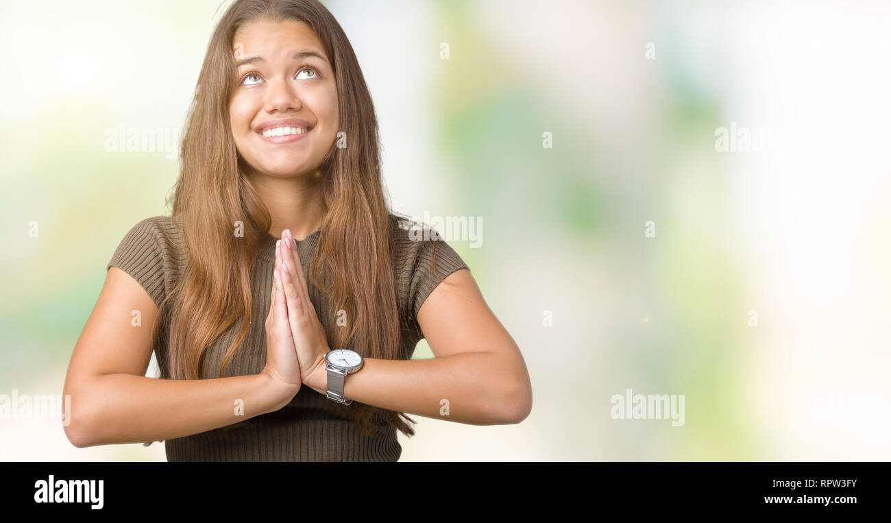Young beautiful brunette woman over isolated background begging and praying with hands together with hope expression on face very emotional and worrie Stock Photo