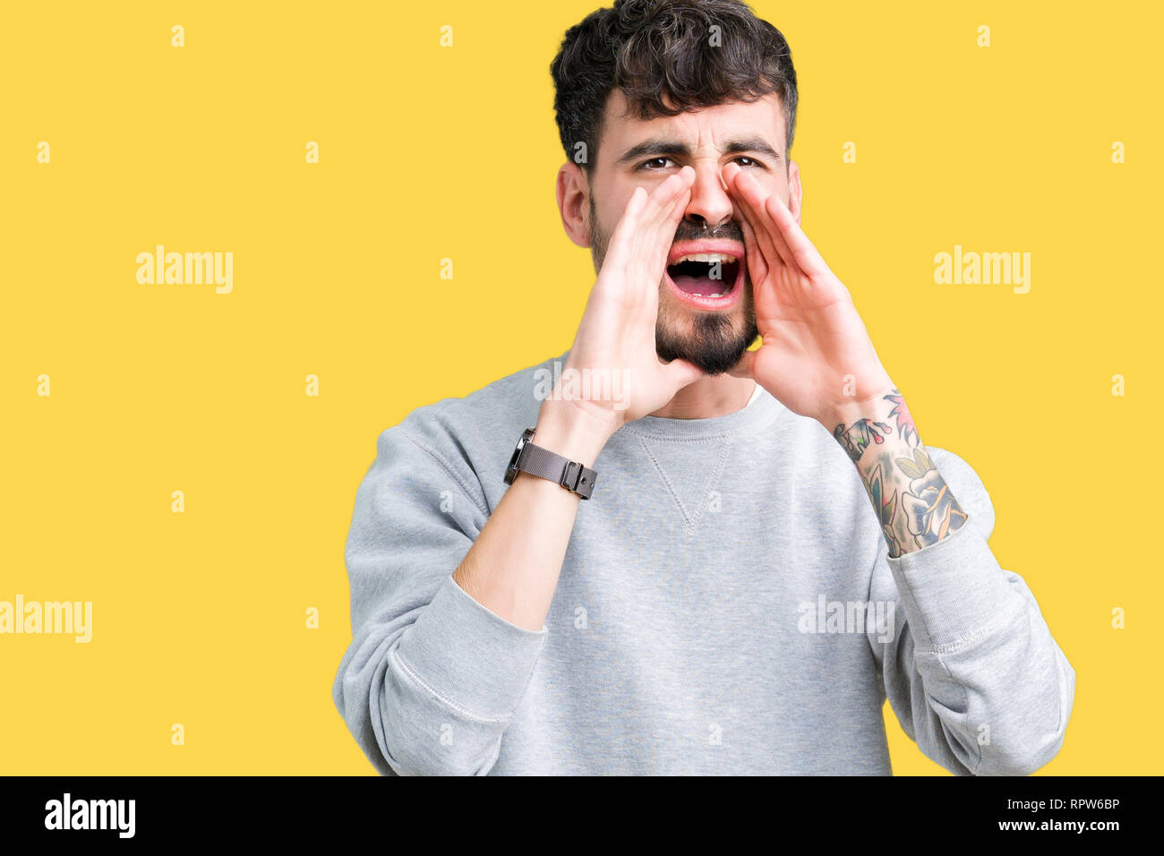 Young handsome man wearing sweatshirt over isolated background Shouting angry out loud with hands over mouth Stock Photo