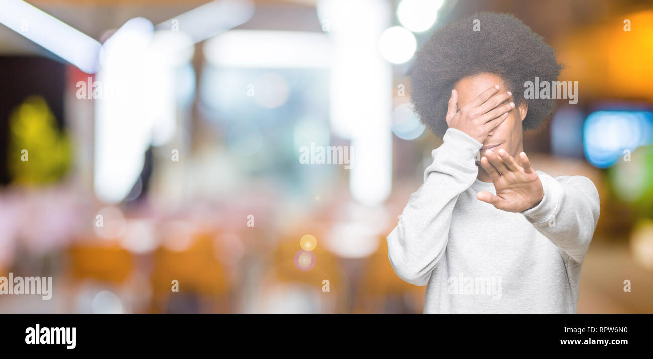 Young african american man with afro hair wearing sporty sweatshirt covering eyes with hands and doing stop gesture with sad and fear expression. Emba Stock Photo