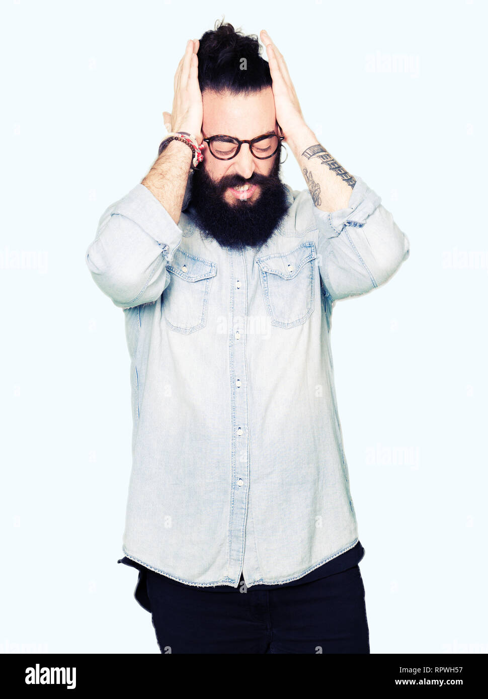 Young hipster man with long hair and beard wearing glasses suffering ...
