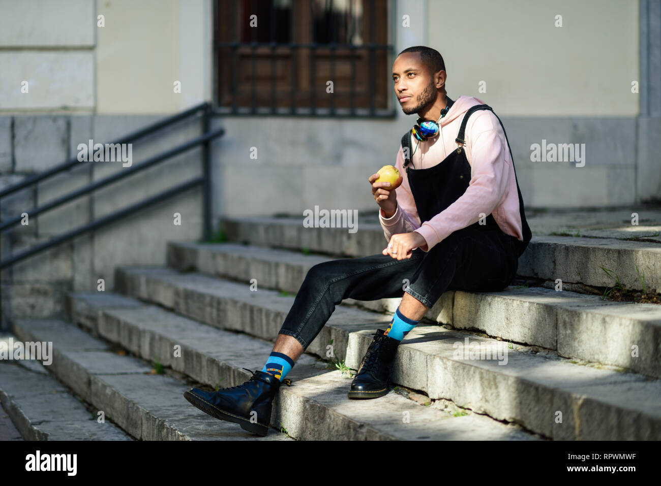 Young black man eating an apple sitting on urban steps.  Stock Photo