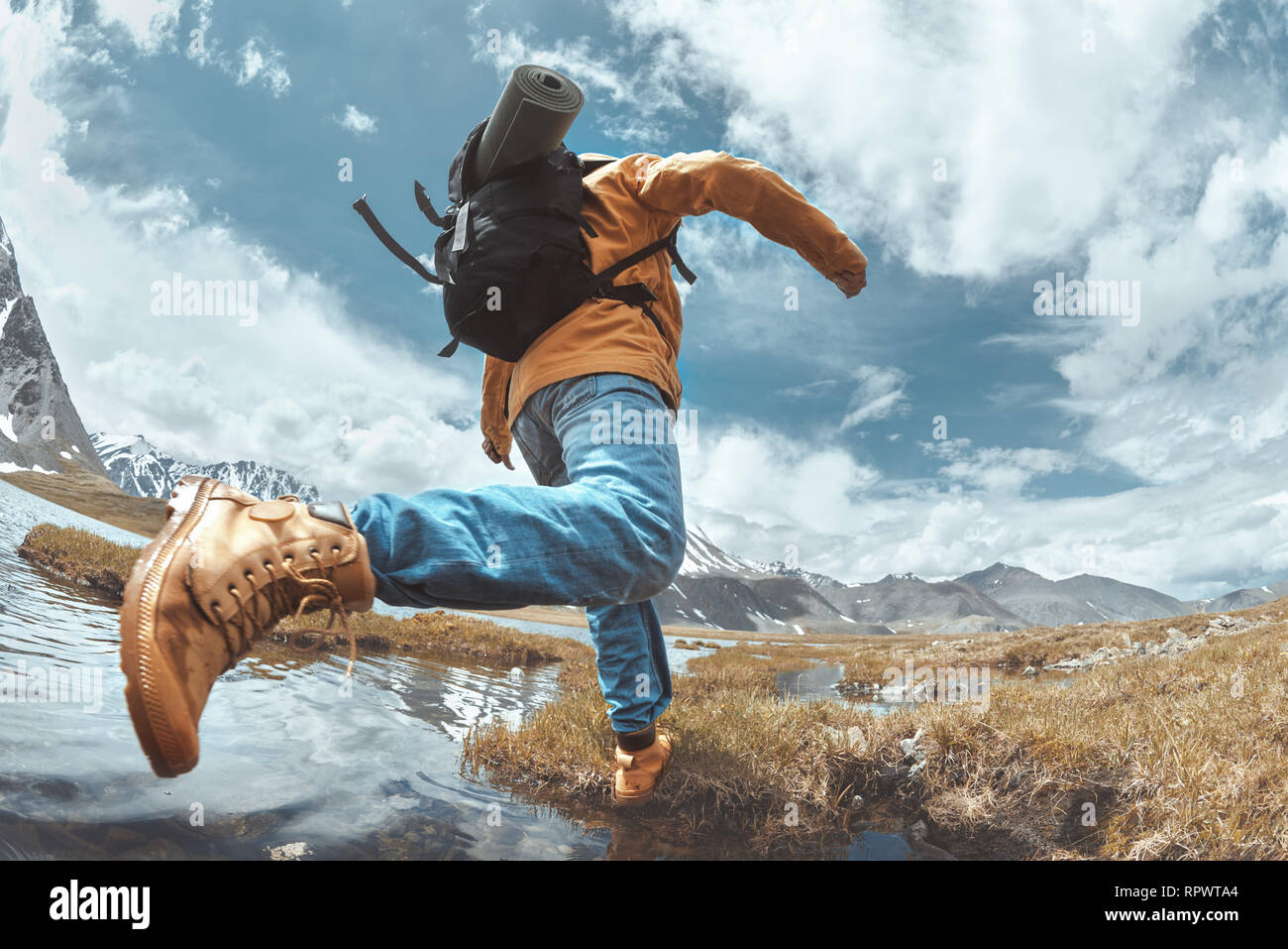 Hiker jumps across water in mountains area. Hiking concept with man Stock Photo