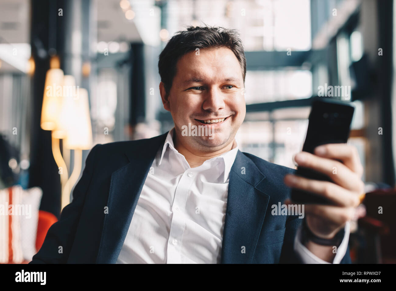 Close-up of attractive young man having a video call in a cafe bar during a break from work, smiling and looking at the camera on his smartphone. Stock Photo