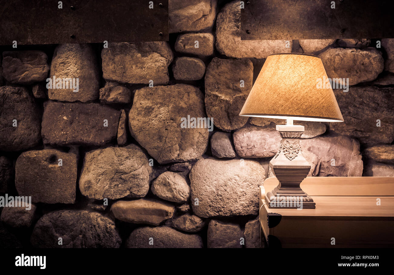 Stone wall illuminated by stylish lamp on wooden table Stock Photo