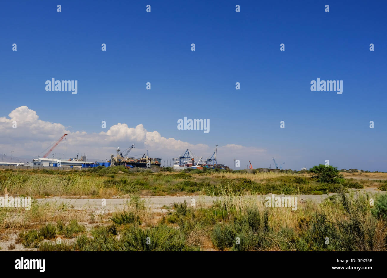 Limassol, Cyprus - June. 23, 2018: View of Limassol docks taken from the wild grass land of Lady's Mile.  Taken on a bright blue sky summer's afternoo Stock Photo
