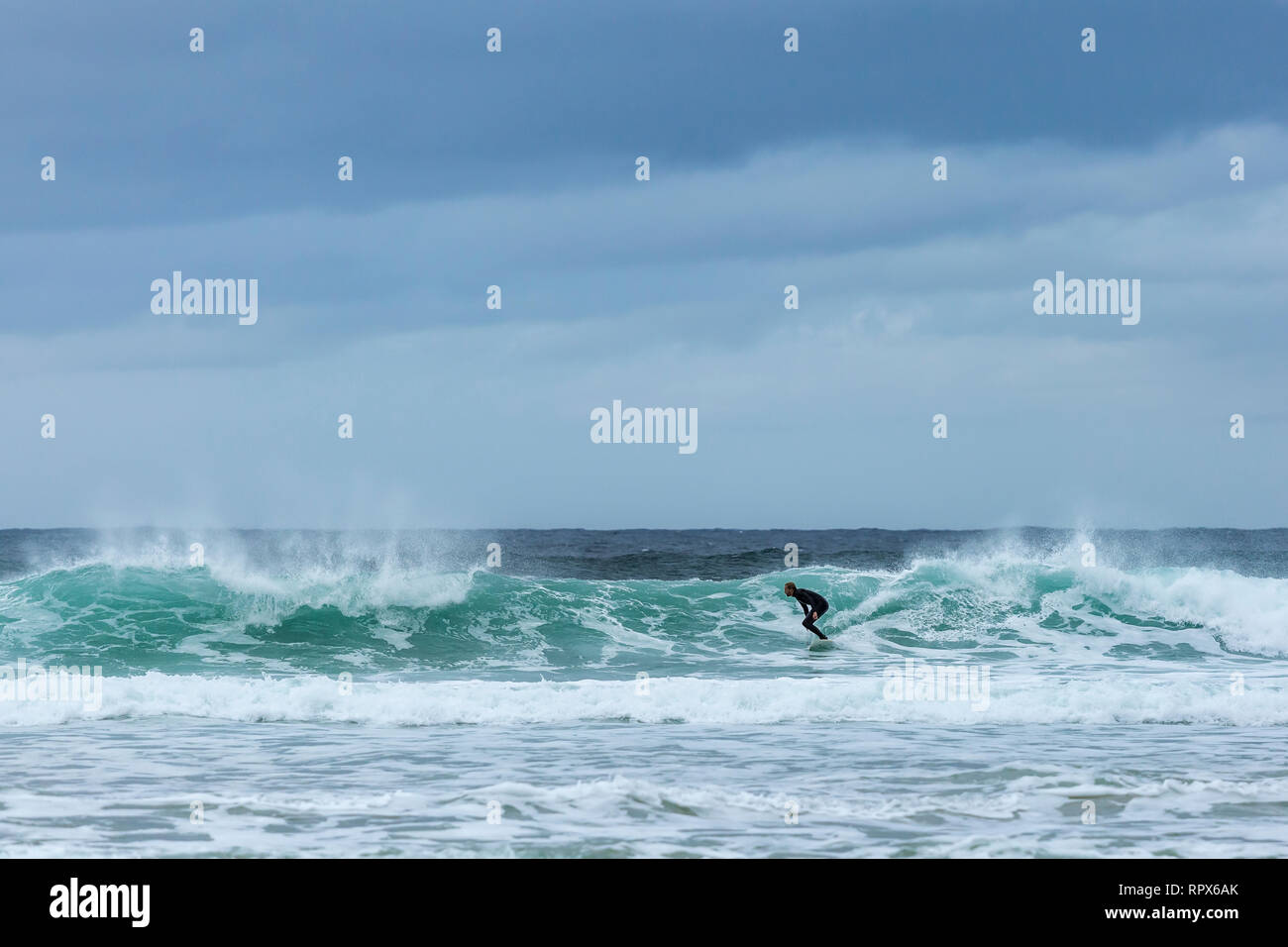 Male surfer in wet suit riding a wave on Dalmore beach Isle of