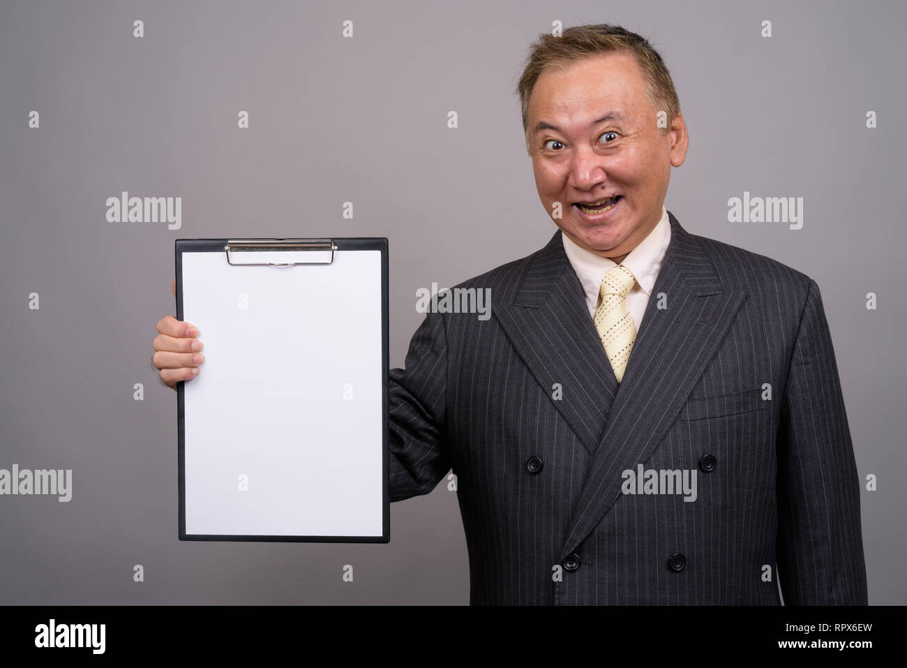 Studio shot of mature Asian businessman holding clipboard against gray ...