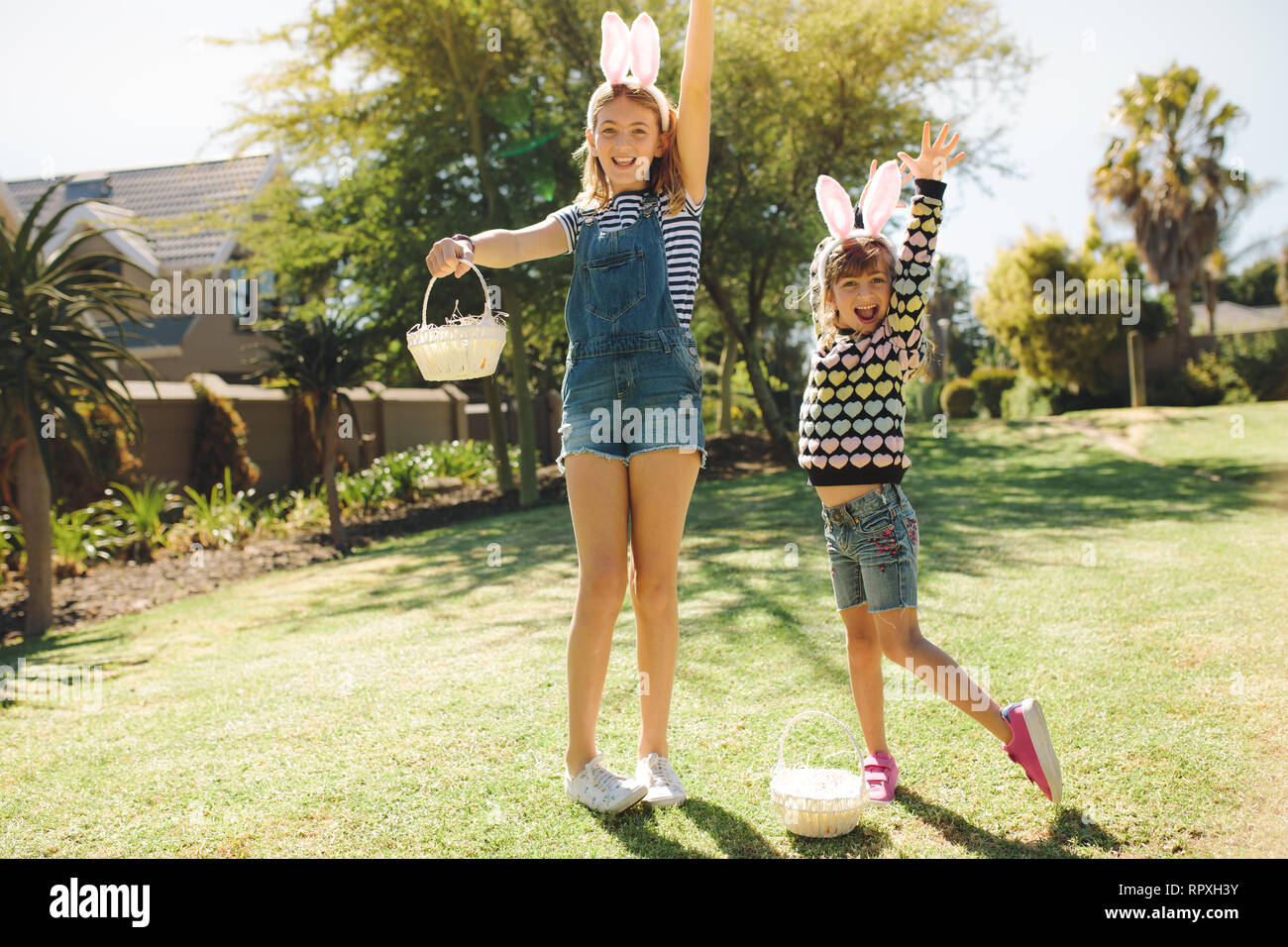 Two kids playing in a garden holding baskets. Girls wearing fancy rabbit ear headband and playing outdoors on a sunny day. Stock Photo