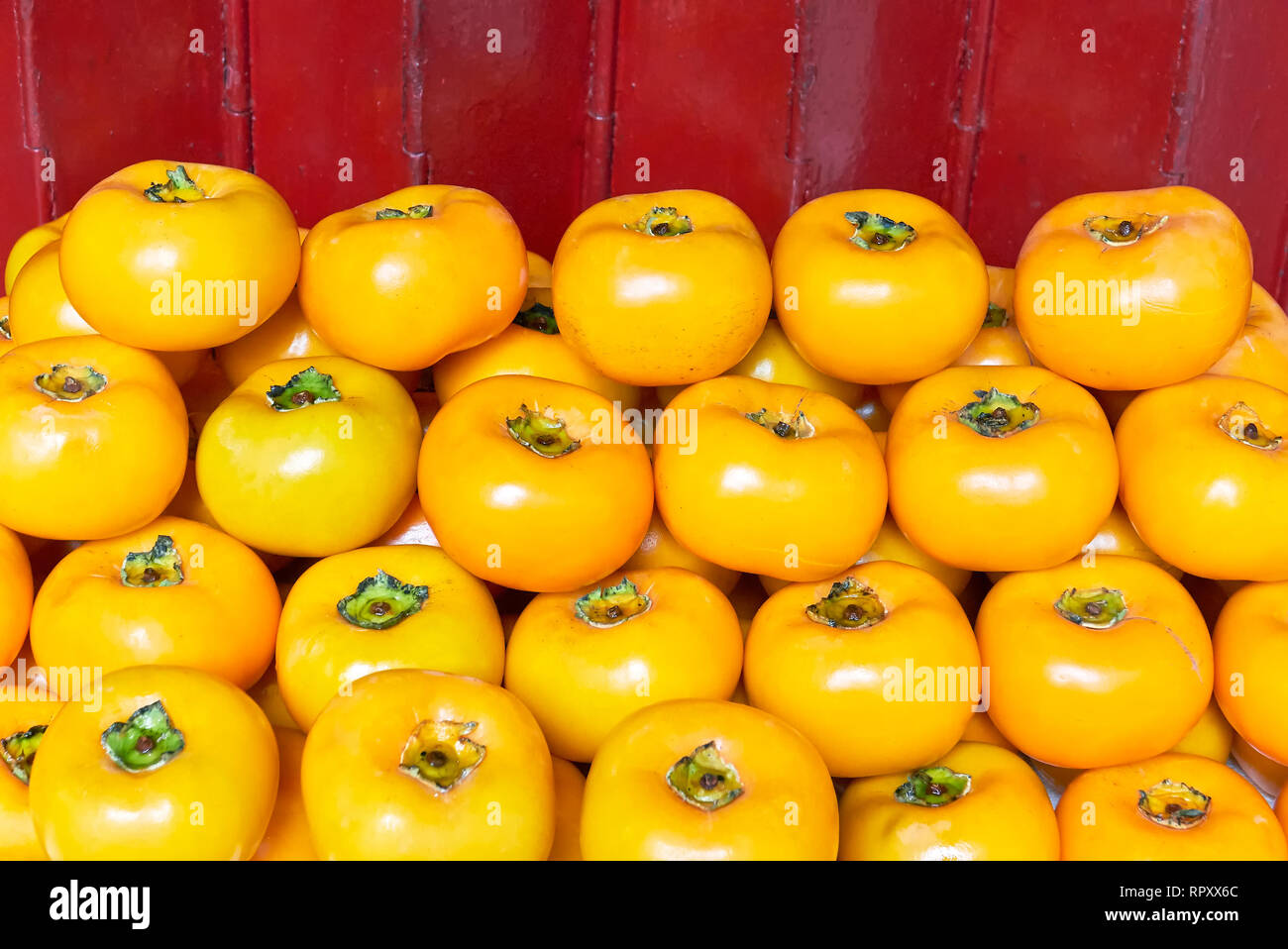 Close-up of a pile of edible orange colored persimmon fruits in front of a red colored background, for sale in Chinatown Manila, Philippines Stock Photo