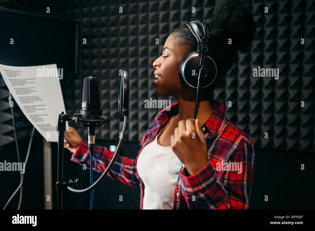 Young woman in headphones songs in audio recording studio. Musician  listens composition, professional music mixing Stock Photo