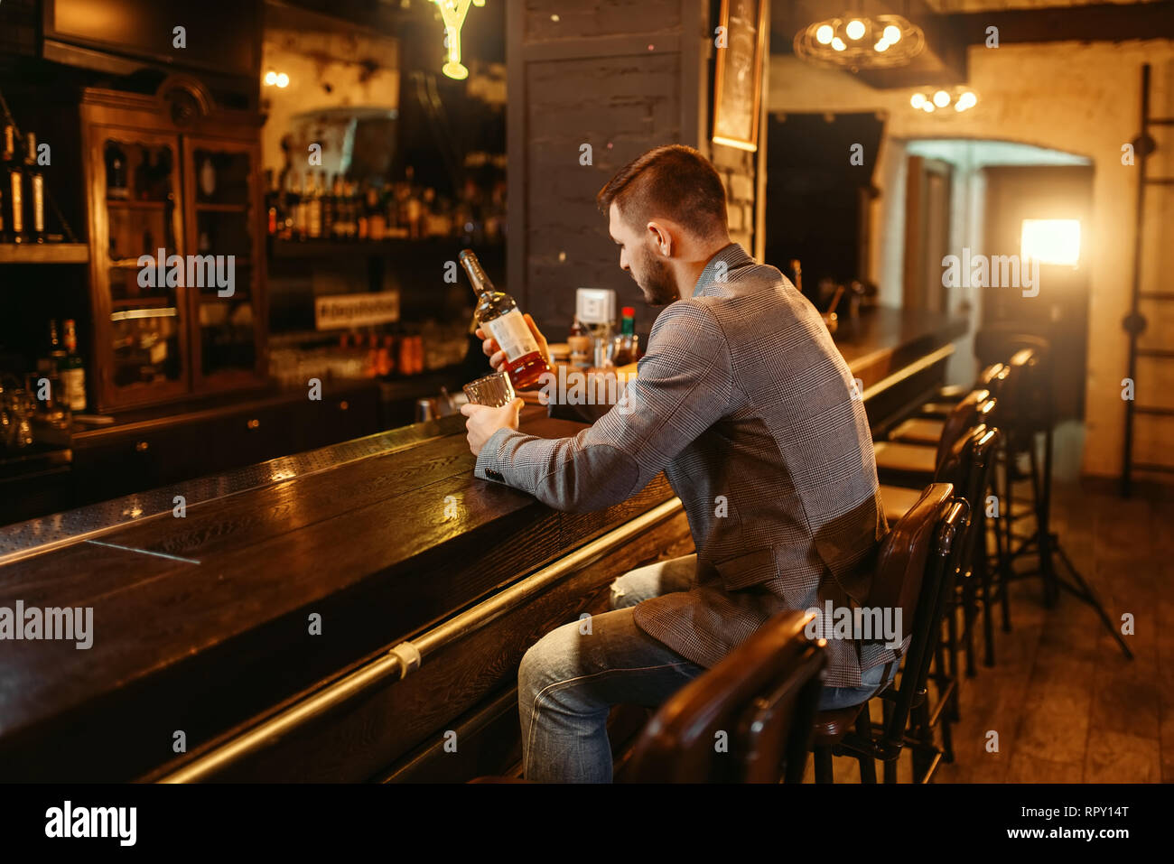 Man with bottle of alcohol beverage drinks at wooden bar counter ...