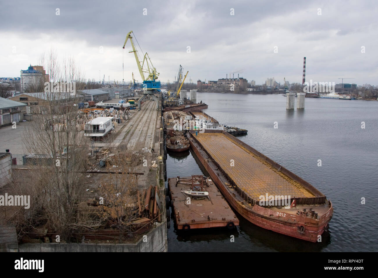 A walk on a cloudy day along the embankment and industrial places of the city along the river, barges, bridges, graffiti, cranes and ships. Stock Photo