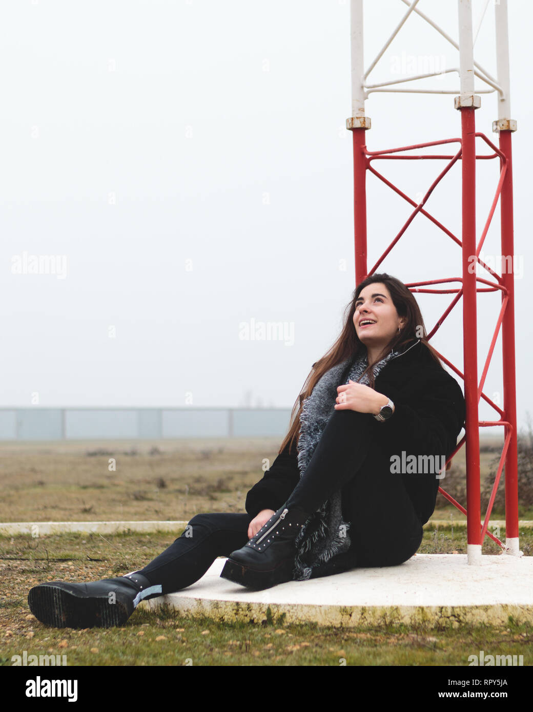 Young beautiful woman sitting on the floor in an small airport looking up in a small airport in a rural landscape. Attractive woman laughing and smili Stock Photo
