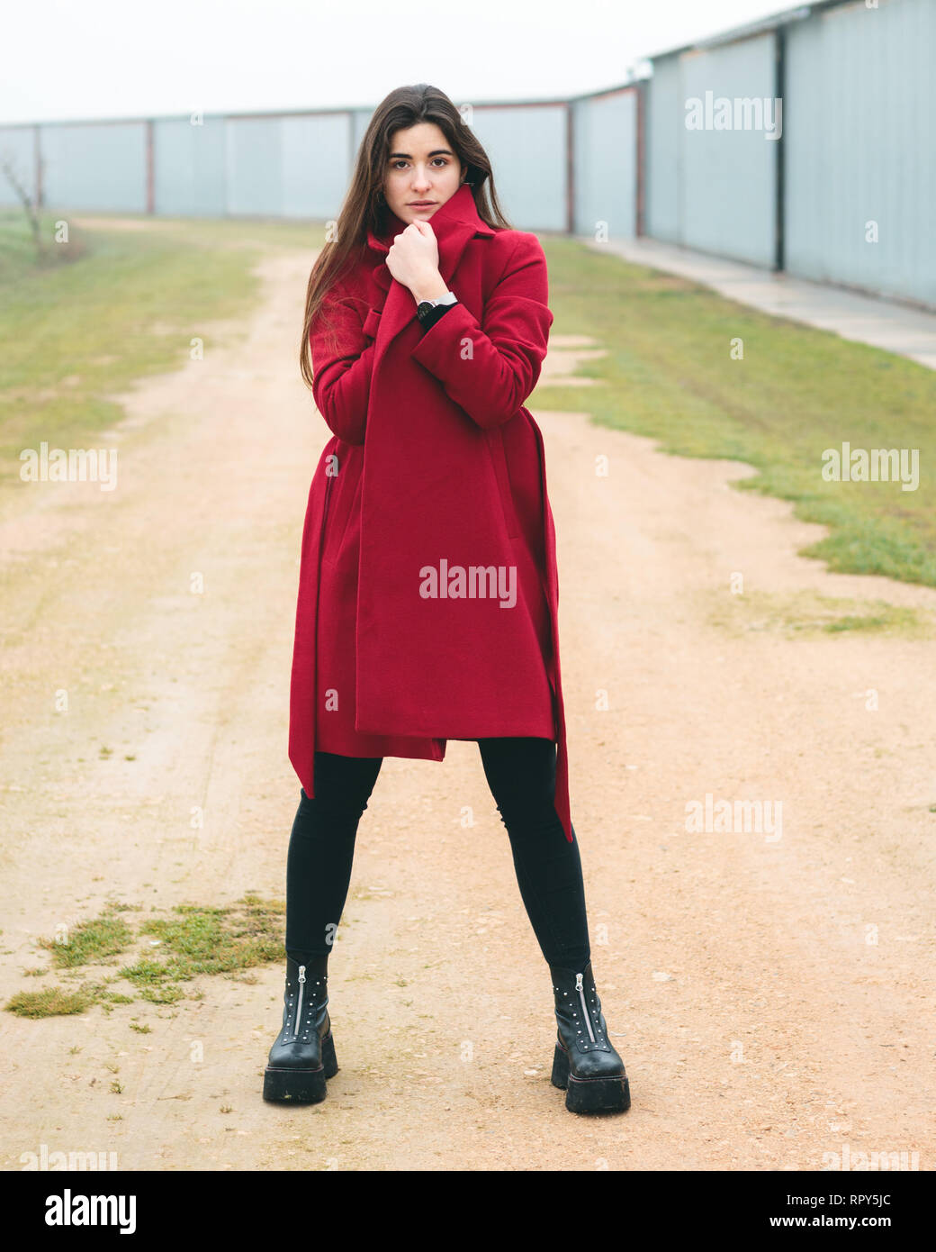 Fashion woman portrait of young pretty girl posing in a rural scene in Europe. Winter and spring fashion, wearing a red jacket. Stock Photo