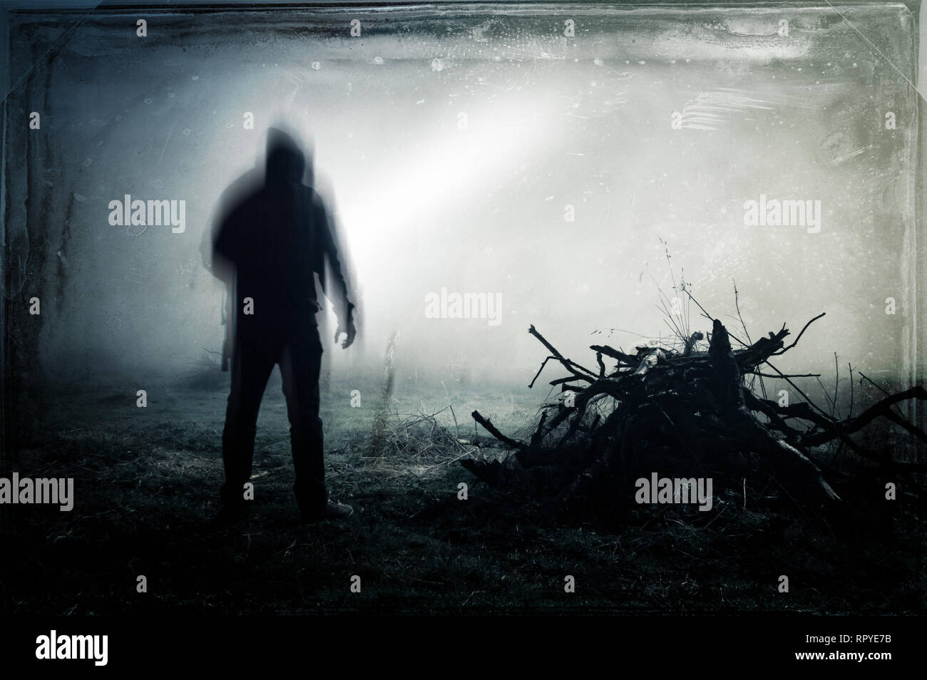 An eerie silhouette of a lone hooded figure in a field With a dark, spooky blurred abstract, grunge effect edit. Stock Photo