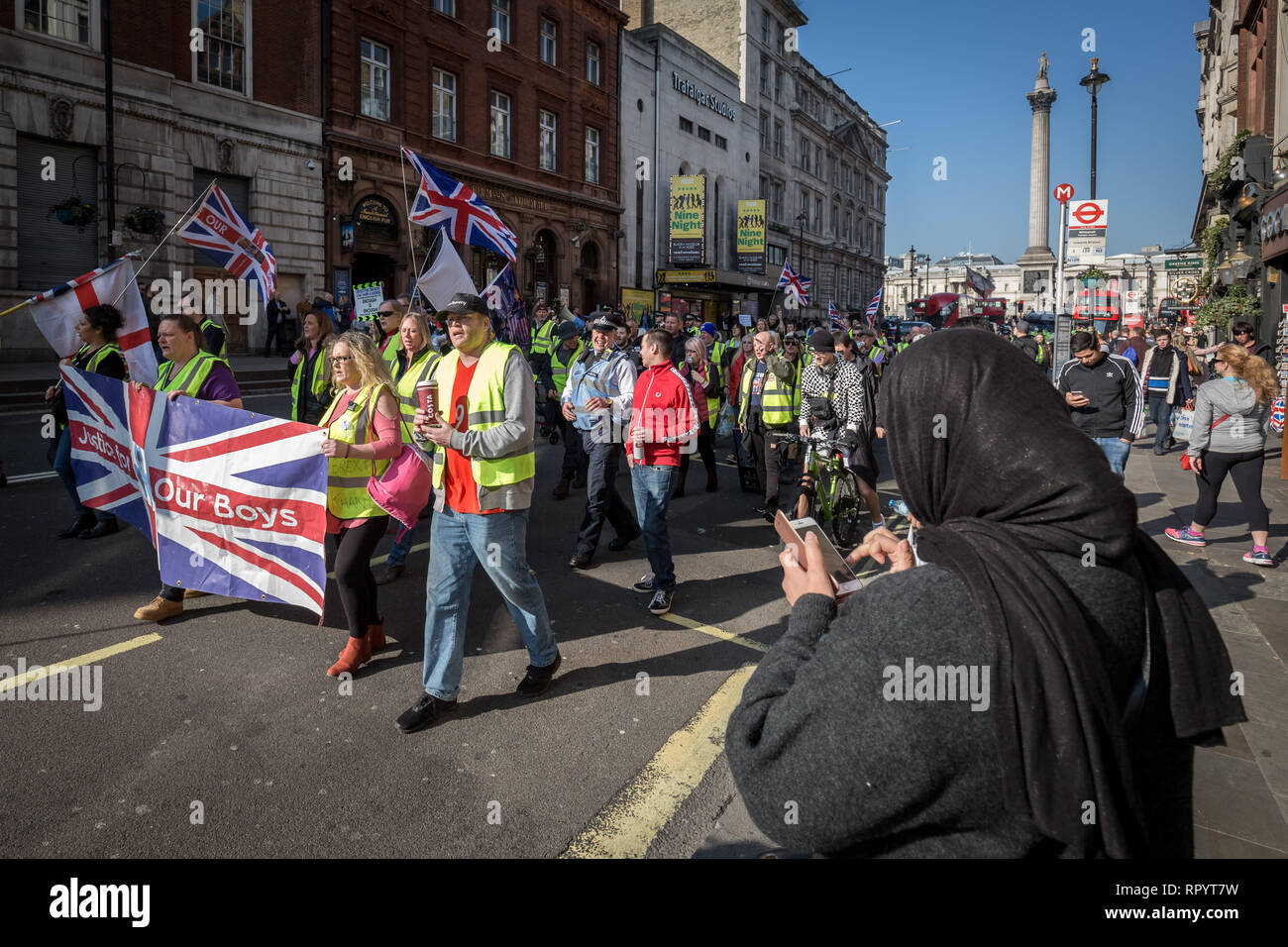 London, UK. 23rd February, 2019. A muslim woman checks her phone as the protesters march down Whitehall. Pro-Brexit protesters calling themselves the 'Yellow Vests UK' movement block roads and traffic whilst protest marching through Westminster. The right-wing nationalists briefly clashed with police and angry drivers whilst aggressively demanding Britain leave the EU without an exit deal. Credit: Guy Corbishley/Alamy Live News Stock Photo
