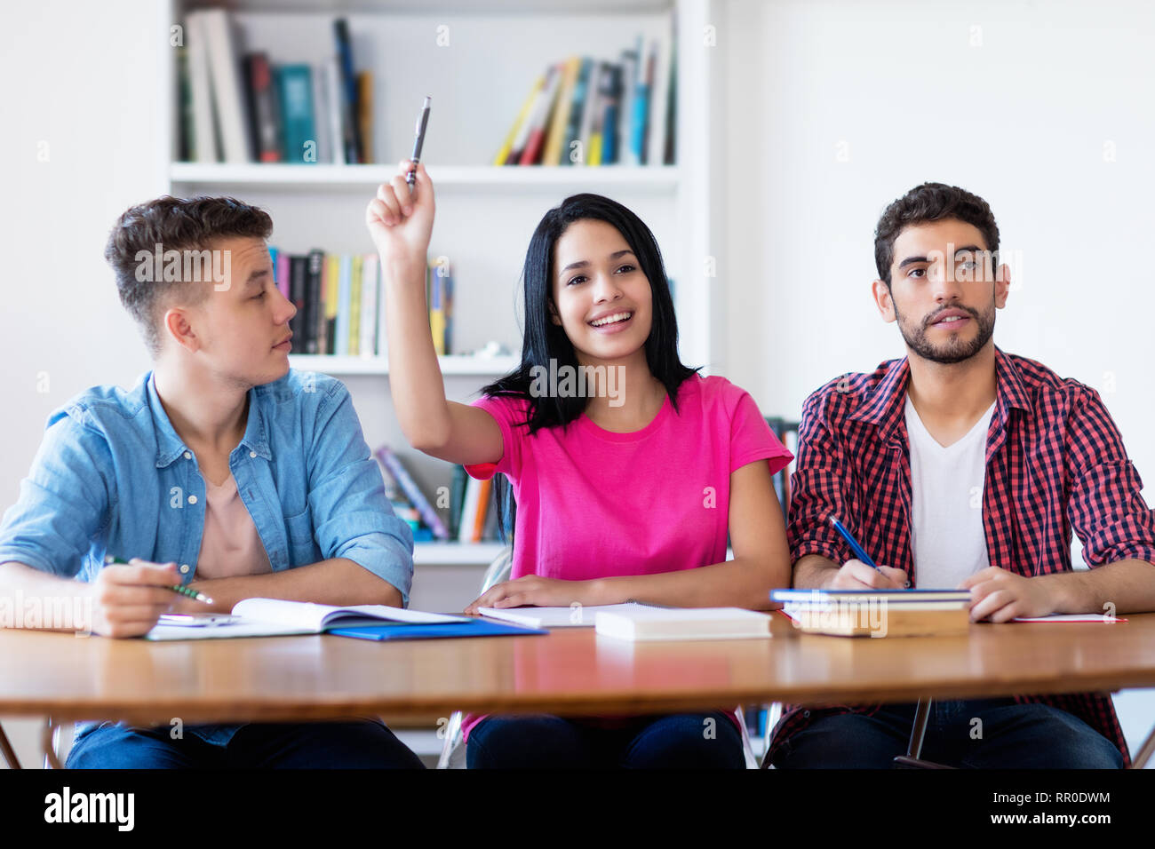 Laughing female student raising hand in classroom of school Stock Photo