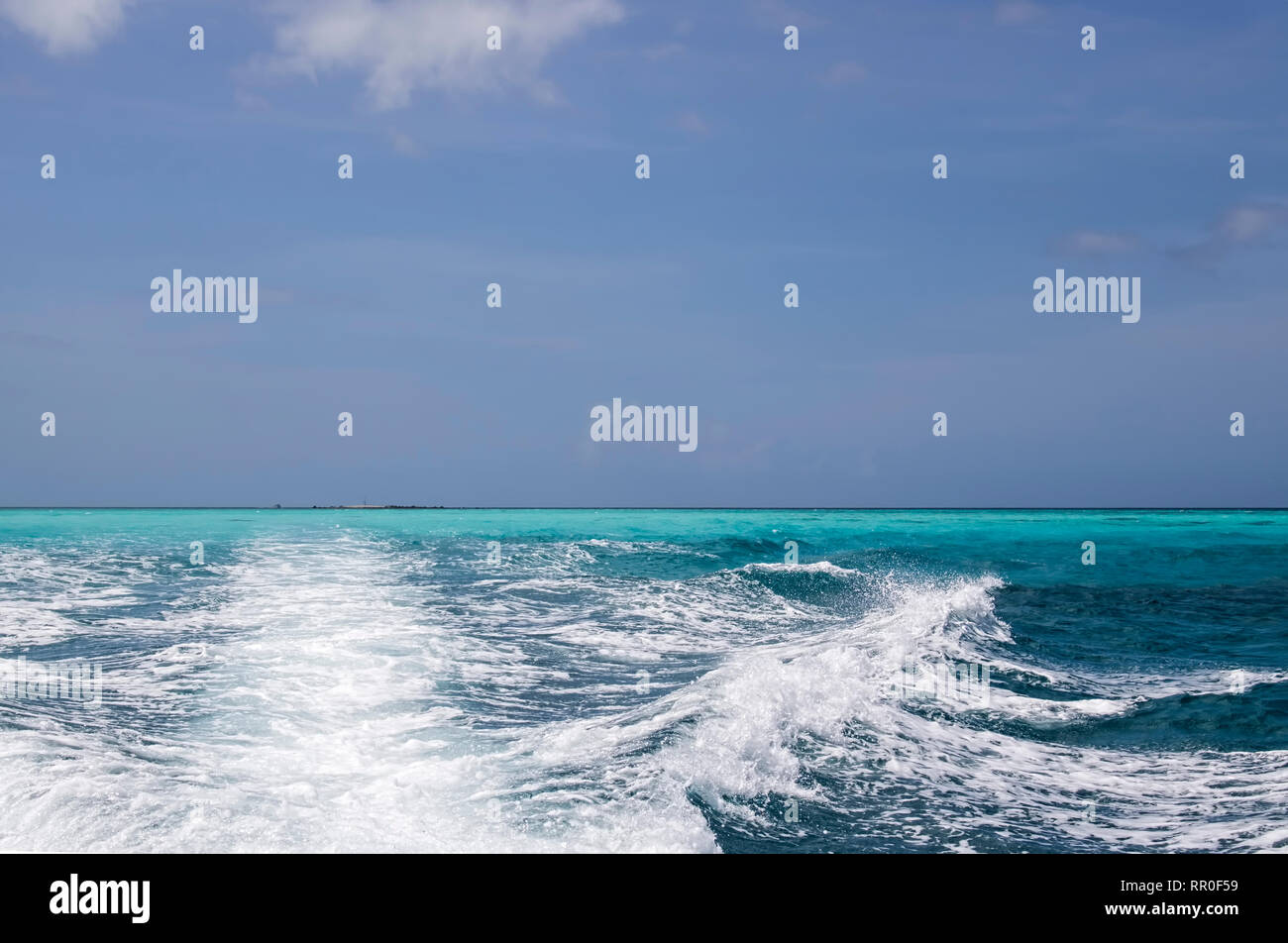 Several shades of blue with white boat wake on ocean surface under blue sky with clouds. Stock Photo