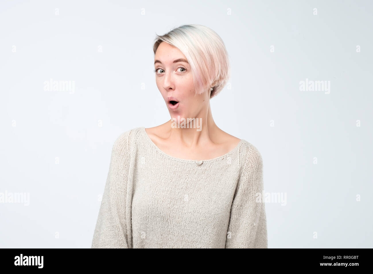 Oh my God concept. Funny european woman with dyed hair and freckles opening mouth widely and popping eyes out in surprise, shocked with some unexpecte Stock Photo