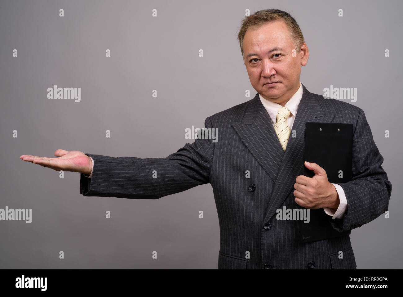 Studio shot of mature Asian businessman holding clipboard against gray ...