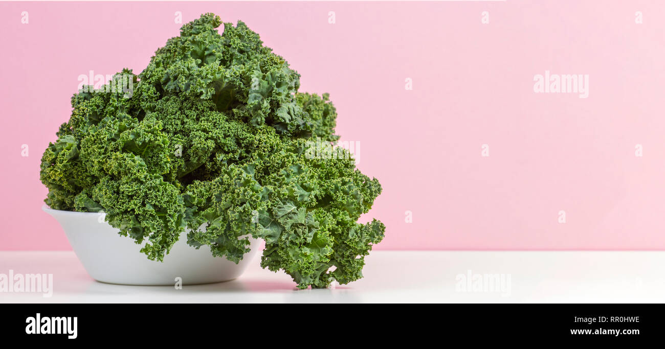 Fresh raw organic green curly kale leaves of kale on white plate with pink background Stock Photo
