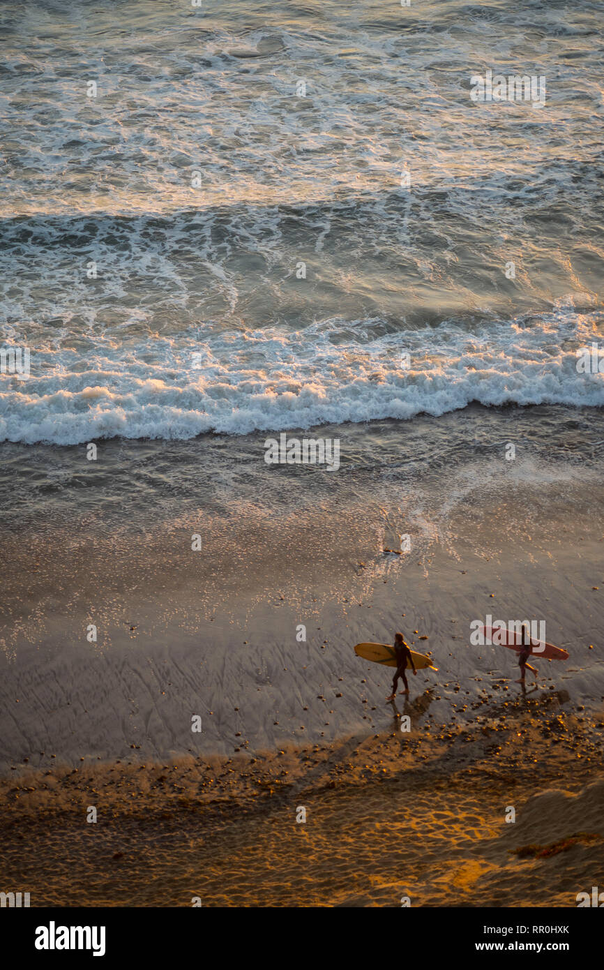 Surfers walking along the beach at sunset in Southern California Stock Photo