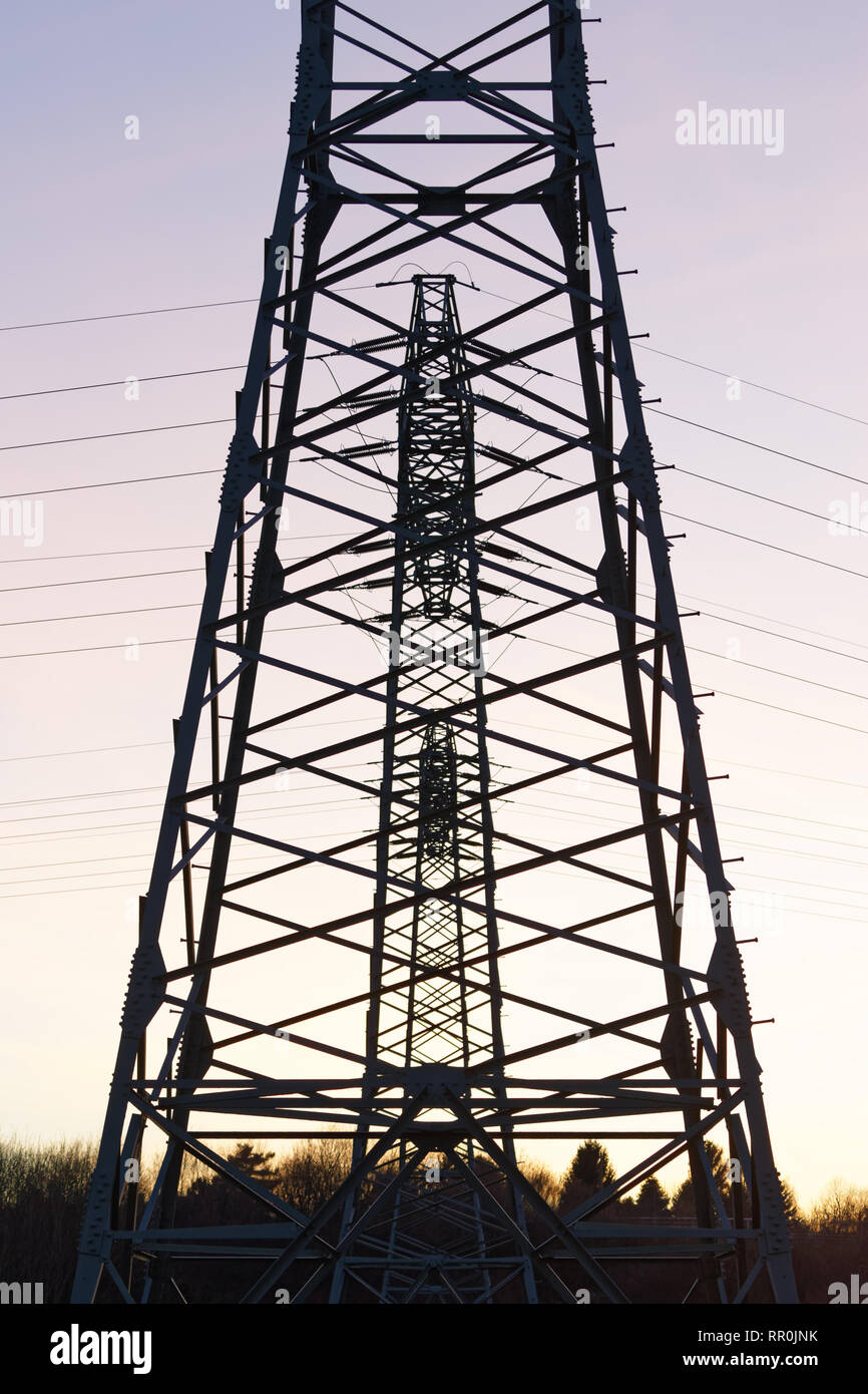 Three electricity pylons are staggered directly behind each other as silhouettes in front of a colored evening sky Stock Photo