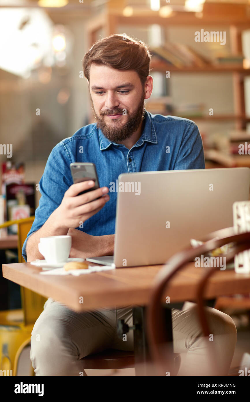 Young man looking at cell phone and work on laptop Stock Photo