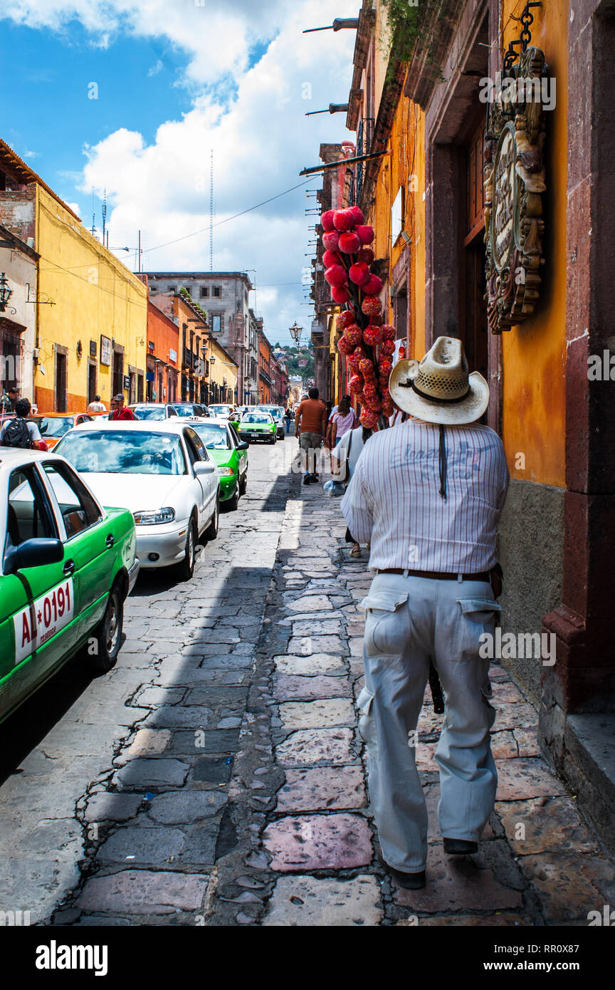 Mexico, San Miguel de Allende busy street scene with candy apple seller walking on cobblestone street. Picturesque town is a popular destination. Stock Photo