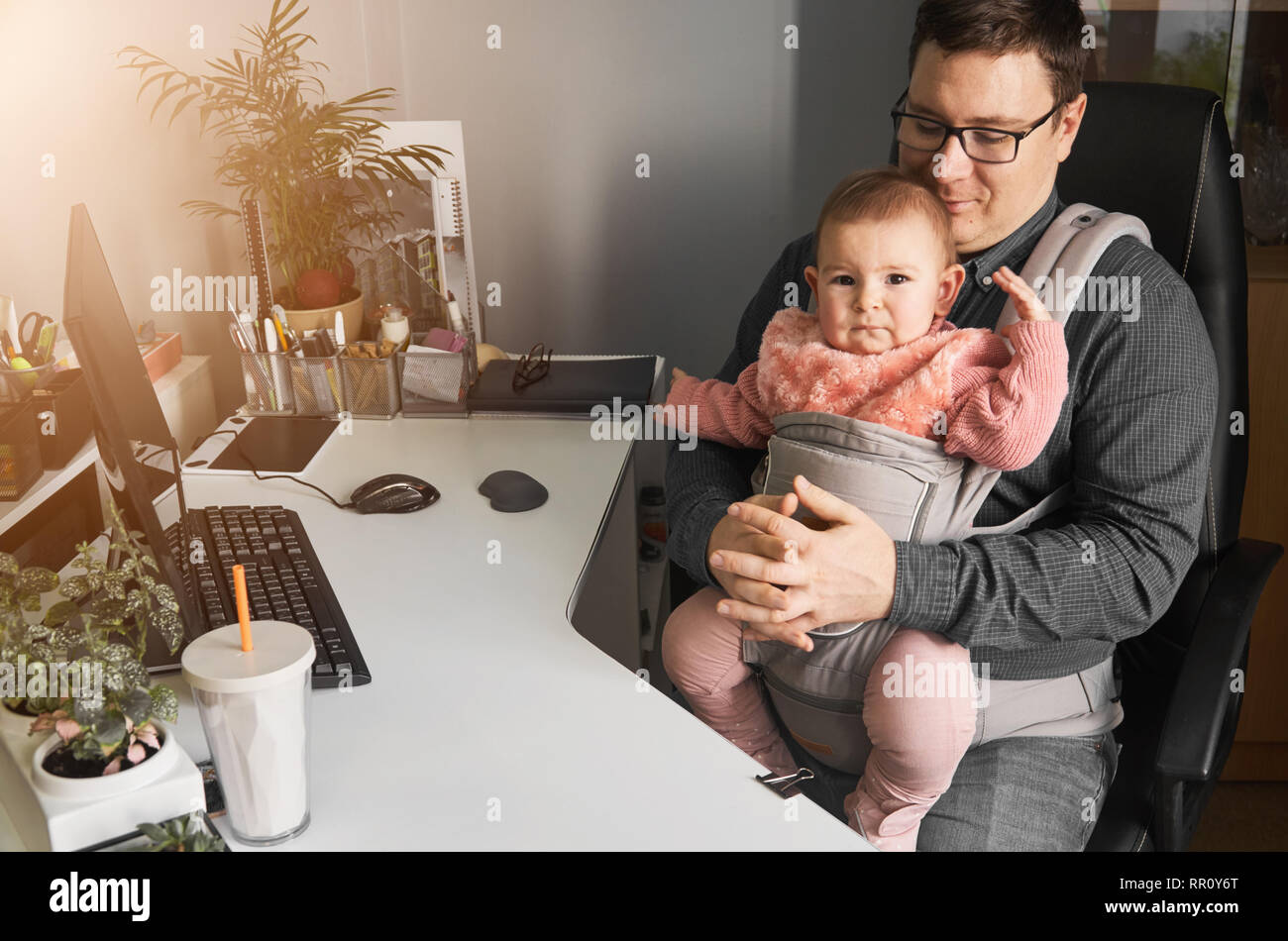 Man father with baby in carrier working at office or home with computer at  the desk, parent in baby friendly office Stock Photo - Alamy