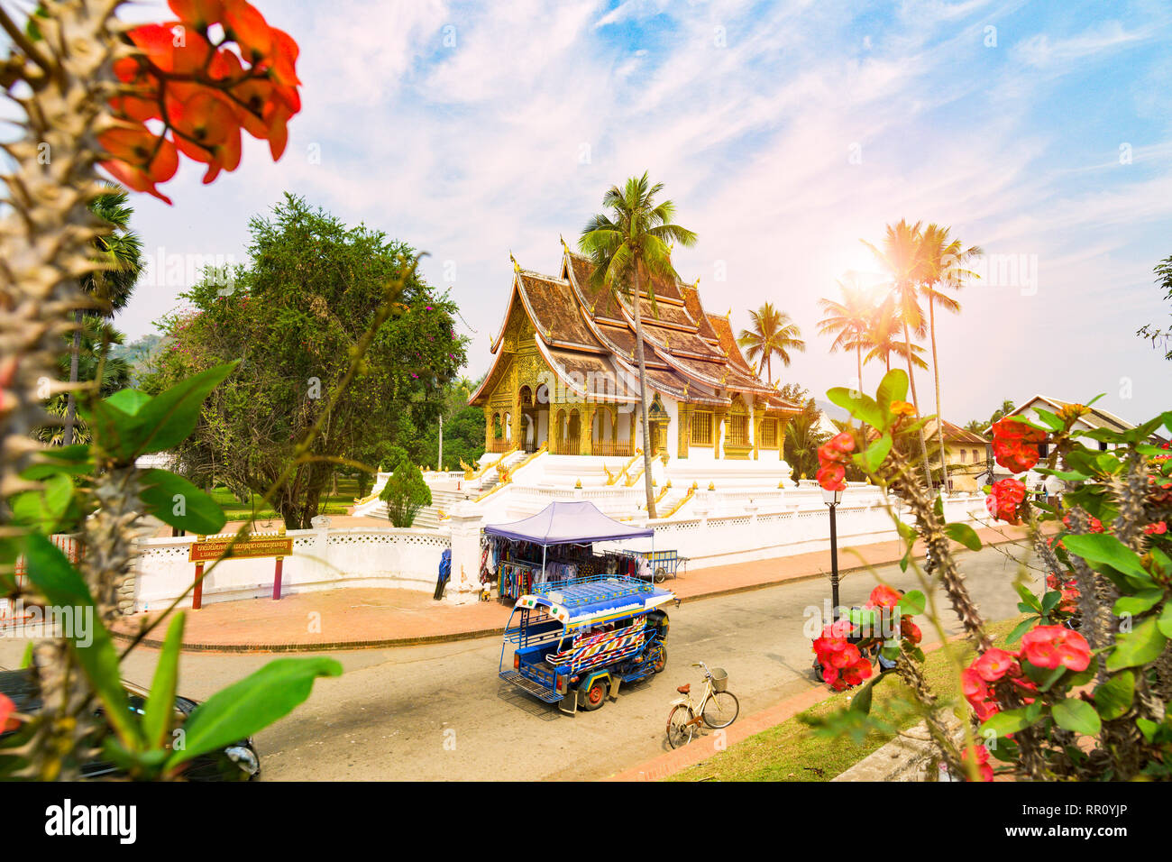 Stunning view of a tuk tuk (auto rickshaw) passing in front of the beautiful Haw Pha Bang Temple. Stock Photo