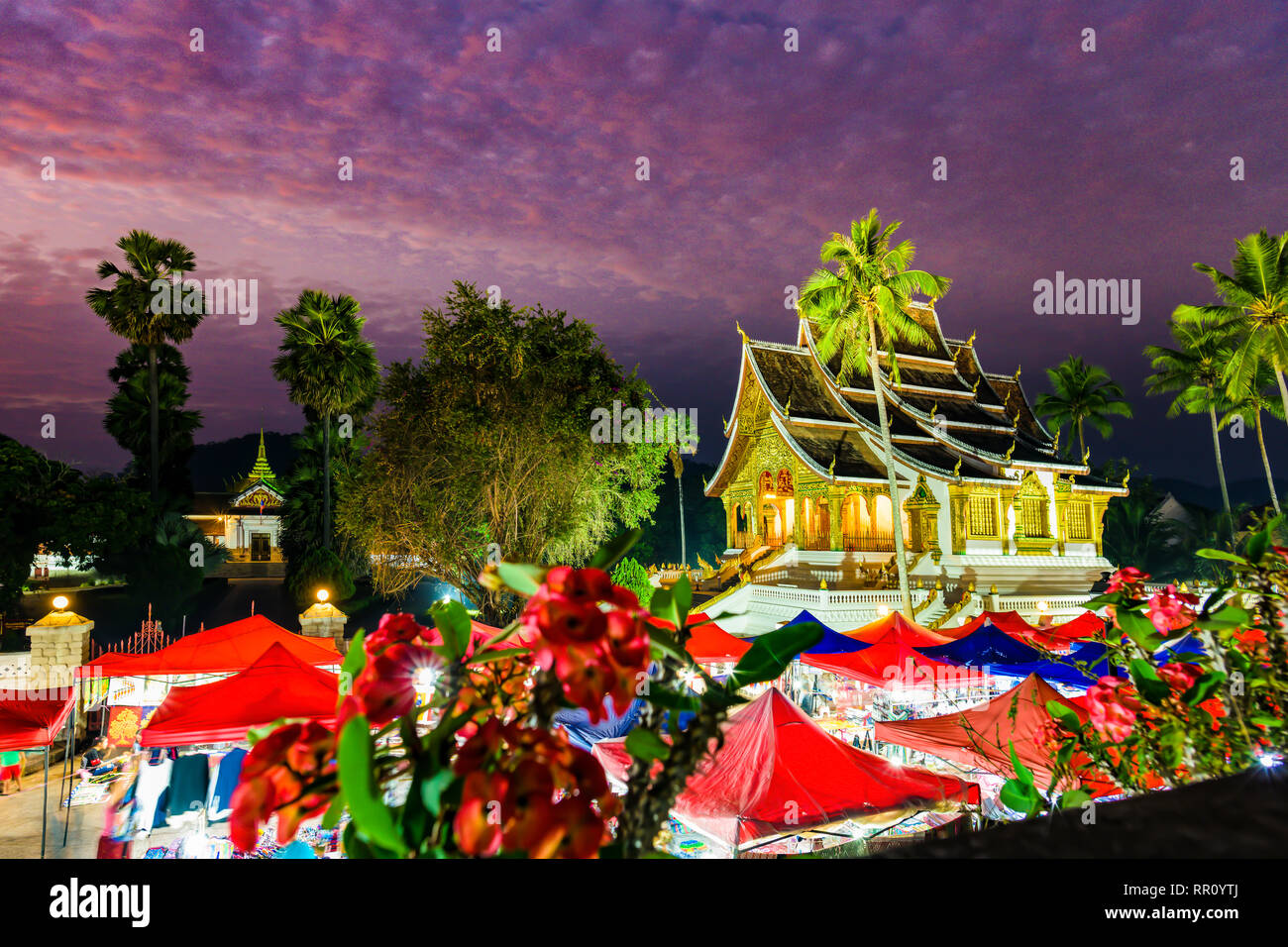 Stunning view of the beautiful Haw Pha Bang Temple at sunset with the illuminated night market curtains in the foreground. Stock Photo