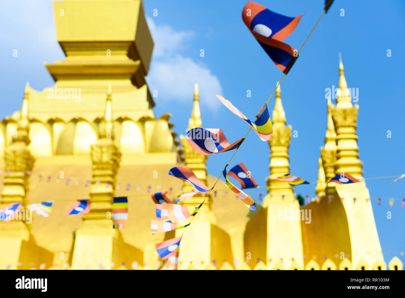 (selective focus) Some Laos flags waving in the foreground with the blurred Pha That Luang in the background. Stock Photo