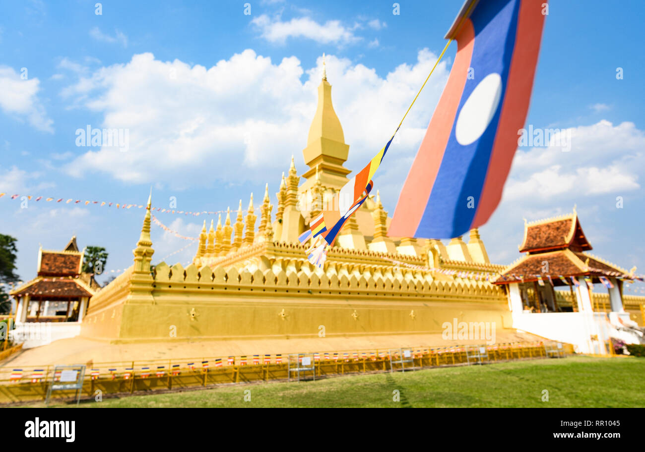 (selective focus) Some Laos flags waving in the foreground with the blurred Pha That Luang in the background. Stock Photo